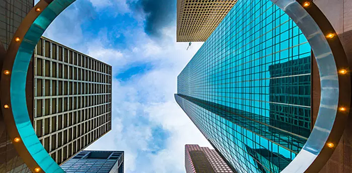Looking up from the ground to a sky view of commercial glass towers and buildings.