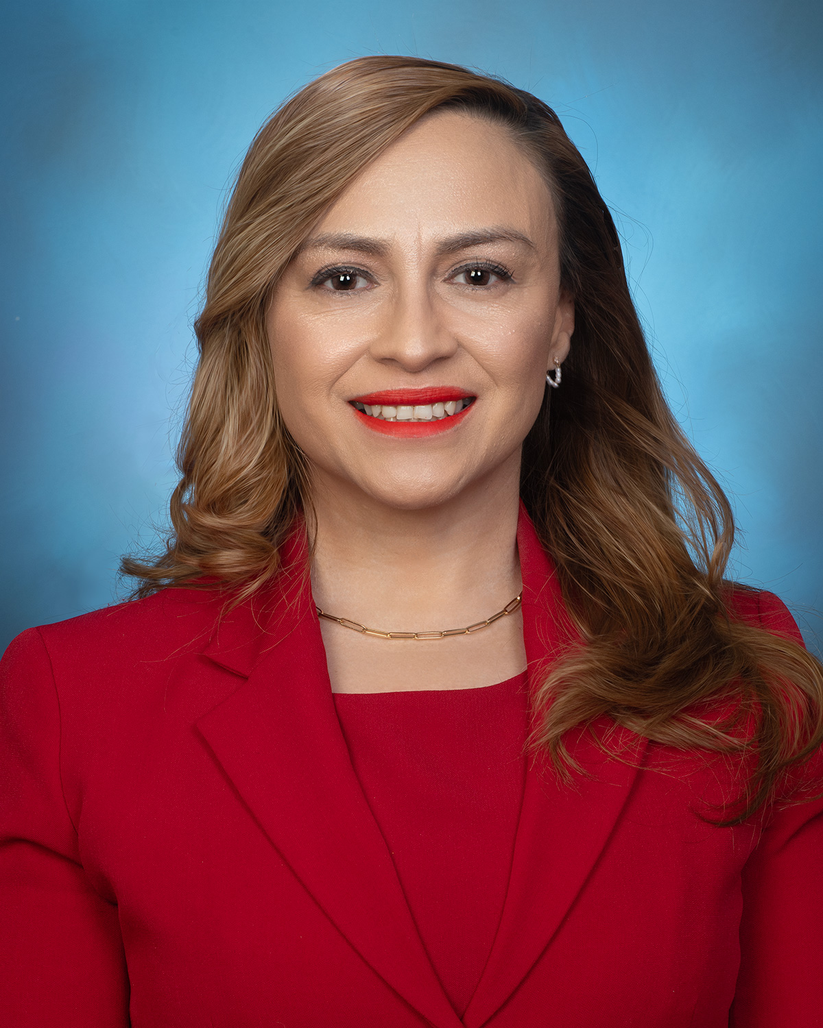 Headshot of a woman smiling wearing a red outfit with a blue background