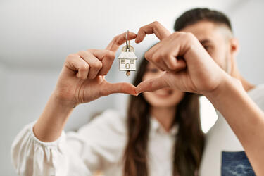 Hispanic couple making a heart with their hands holding house keys