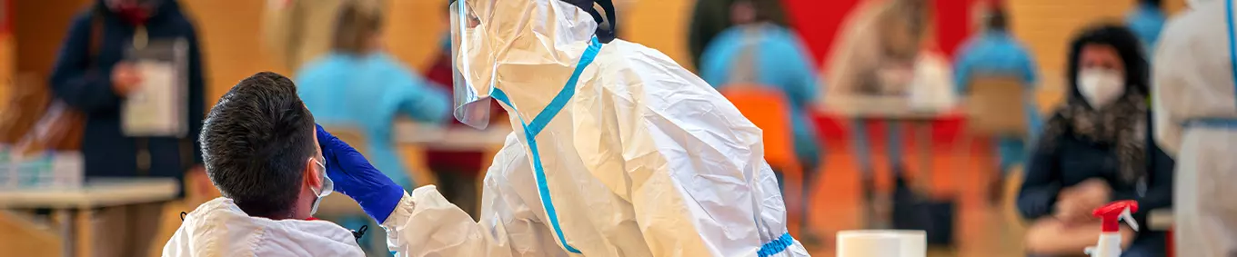 A man in a hazmat suit providing vaccines to people in a gymnasium.