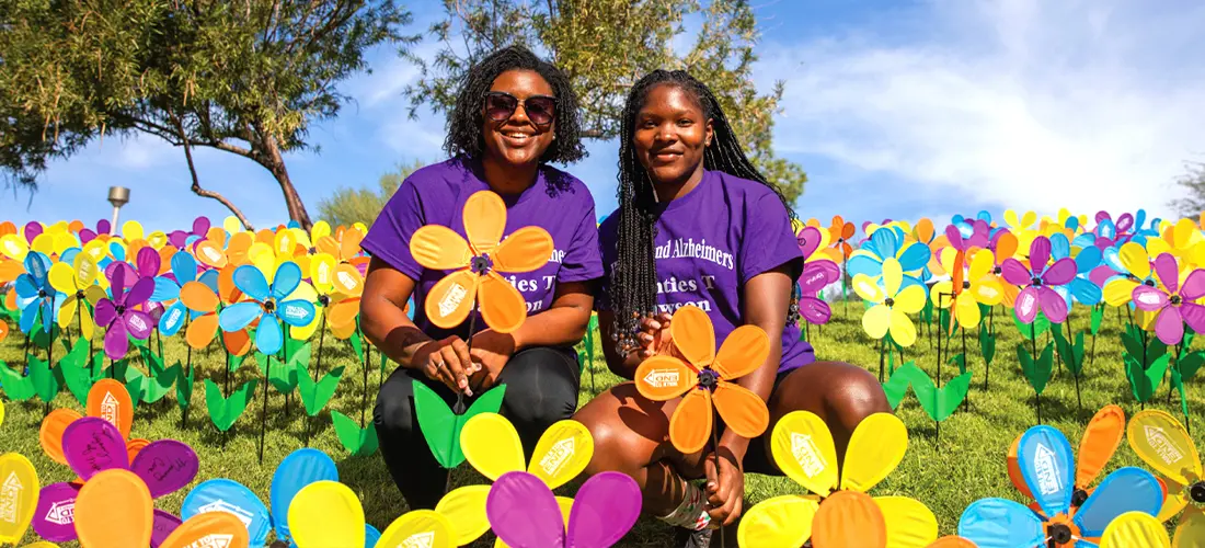 Two black women celebrating the Walk to End Alzheimer's, holding their symbolic Alzheimer's rememberance flowers in various colors.