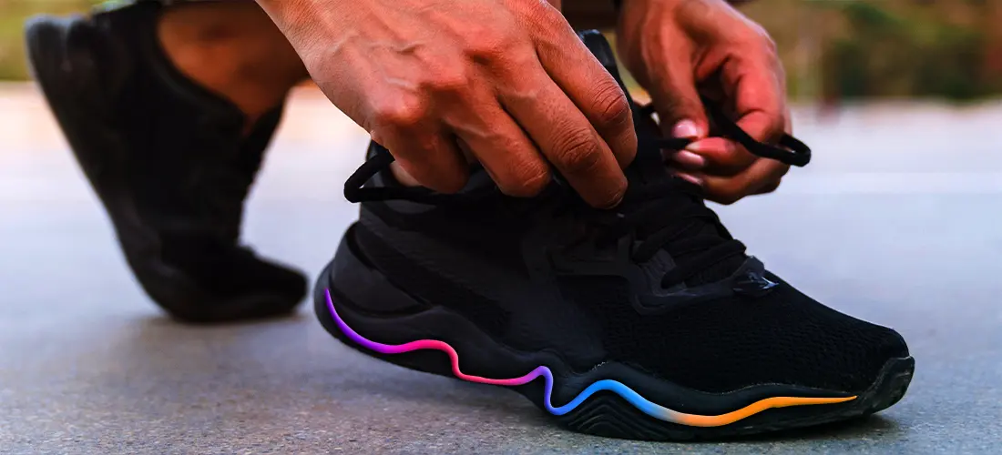 A man lacing up his running sneakers with a colorful stripe on the side, getting ready to take a jog.