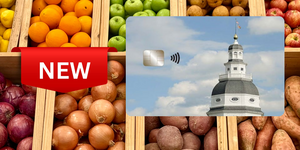 Photo cutout of new Maryland EBT Card on right and "new" flag on left Array of fruits in vegetables in wood containers on display in background