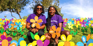 Two black women celebrating the Walk to End Alzheimer's, holding their symbolic Alzheimer's rememberance flowers in various colors.