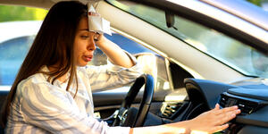 A woman frantically trying to cool down her car with the AC, wiping the sweat off her brow with a napkin in the extreme heat.