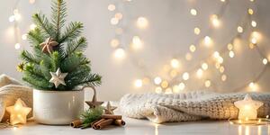 Christmas tree in a mug, Christmas lights, cinnamon sticks, and a blanket all sitting on a table