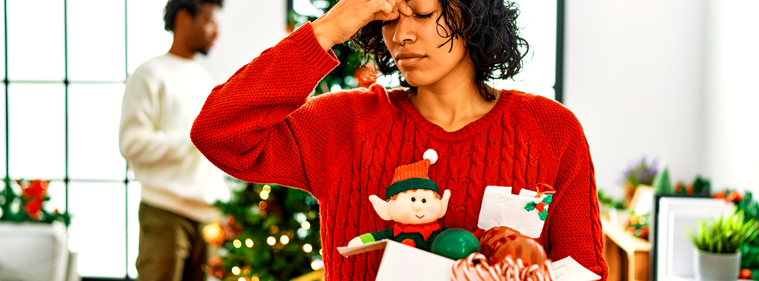 woman in a christmas sweater with her fingers rubbing the bridge of her nose appearing stressed.
